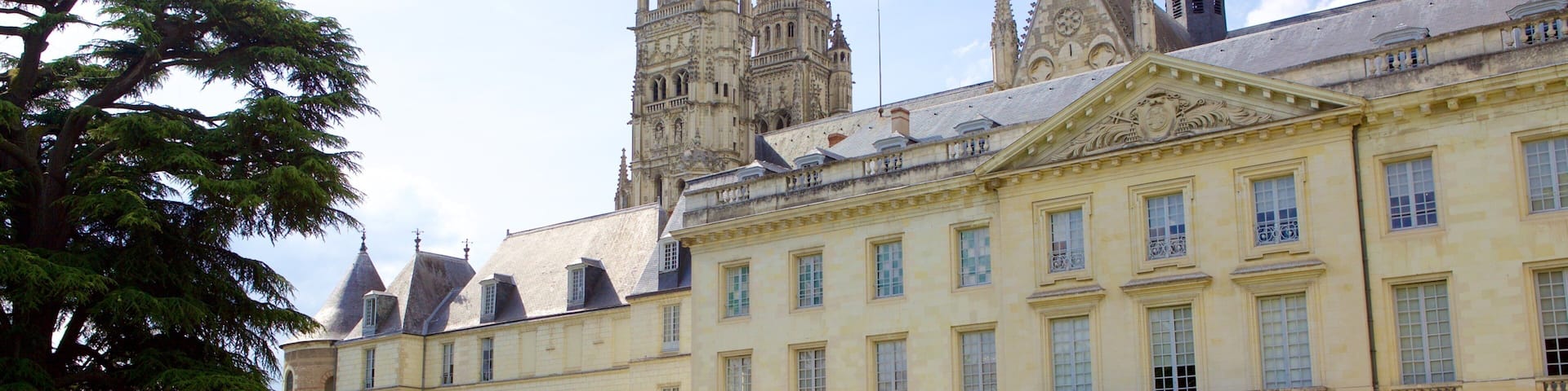 A historic building with a large courtyard, manicured hedges, and a prominent tower in the background.