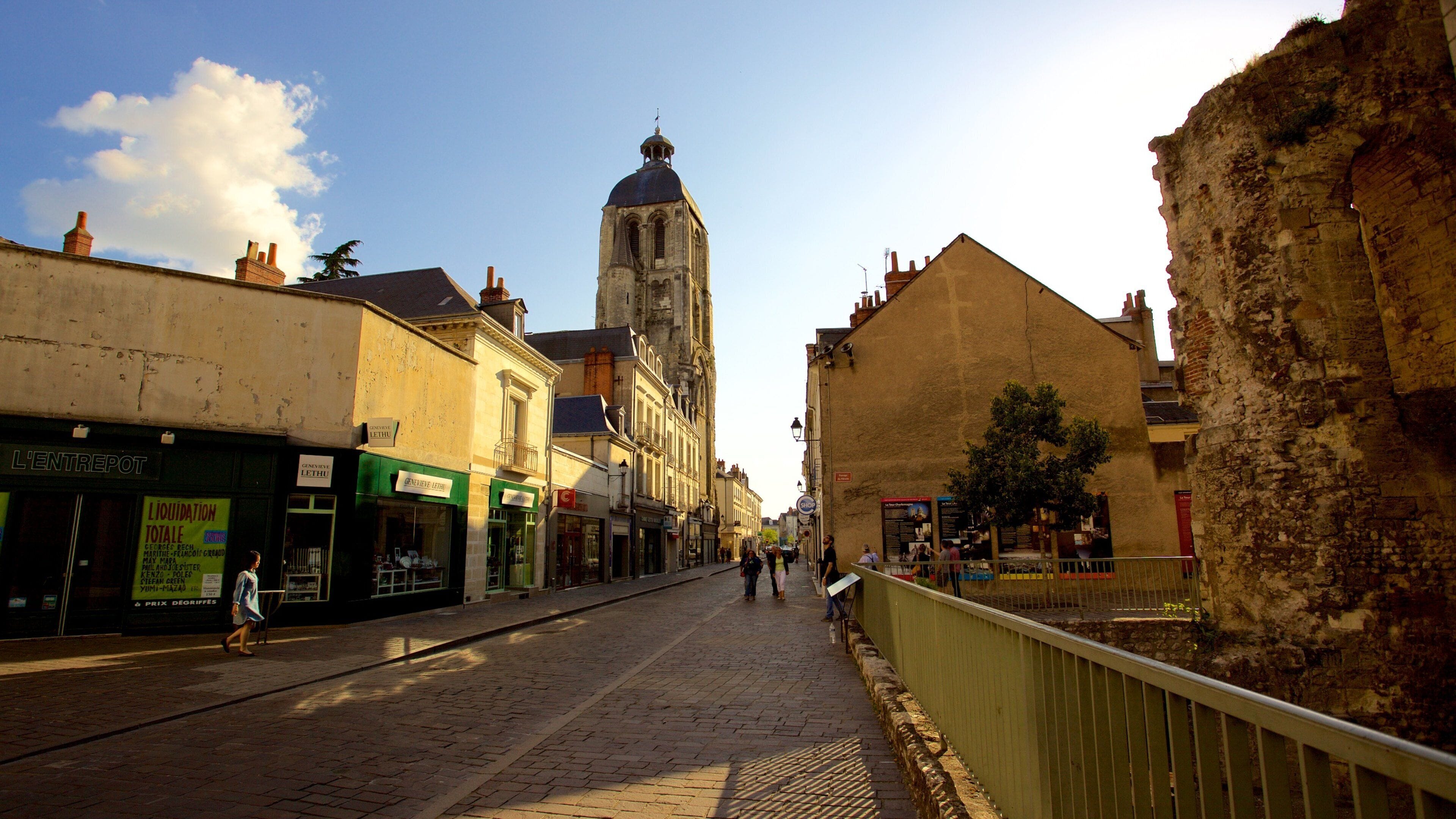 A cobblestone street lined with historic buildings, a prominent tower, and pedestrians.