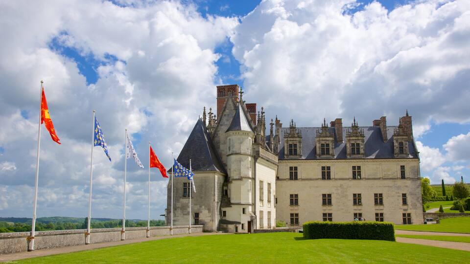 A historic castle with multiple flags, a well-manicured lawn, and a clear sky.