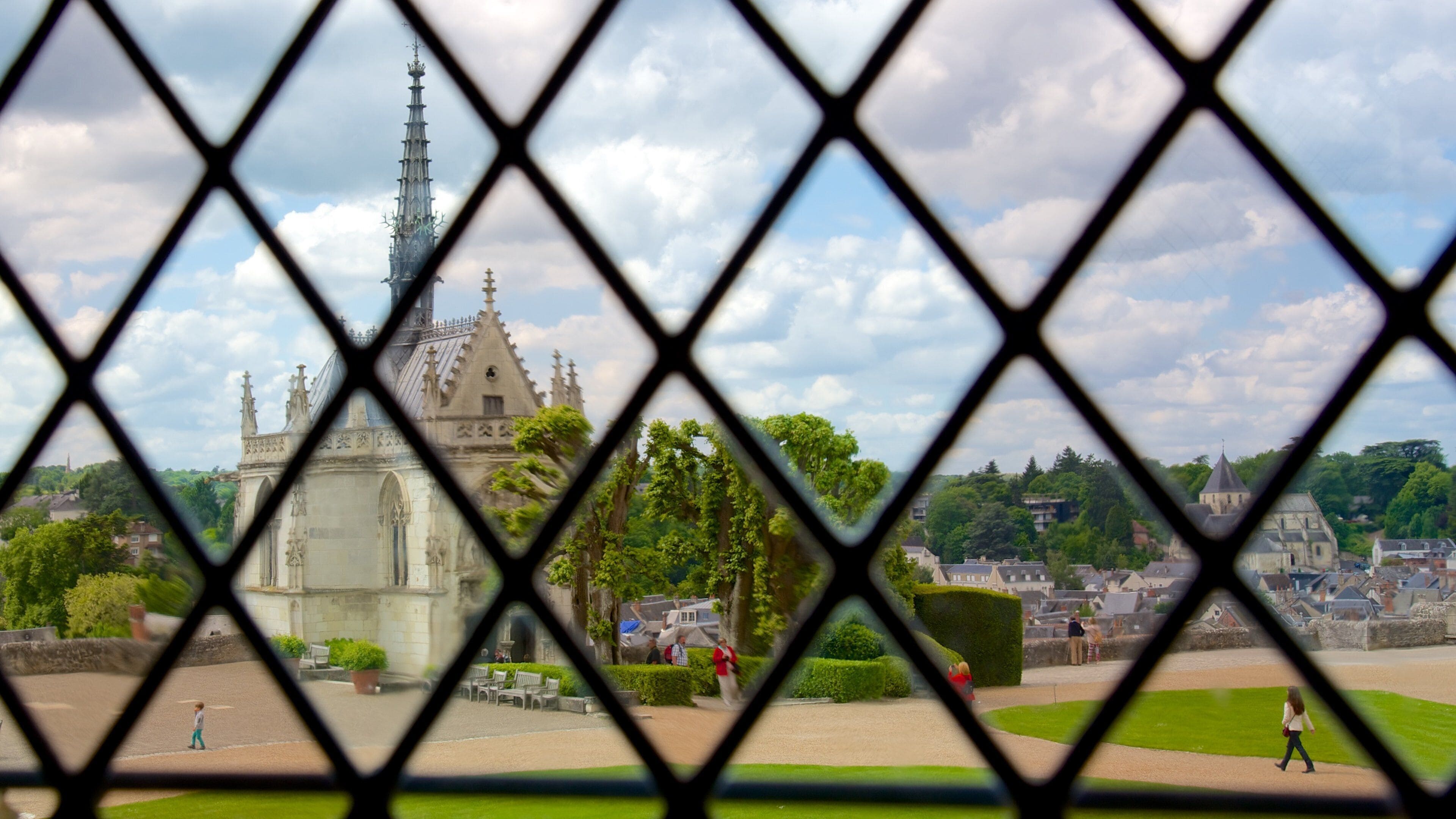 A historic cathedral with a tall spire, surrounded by lush greenery and a small park with benches.