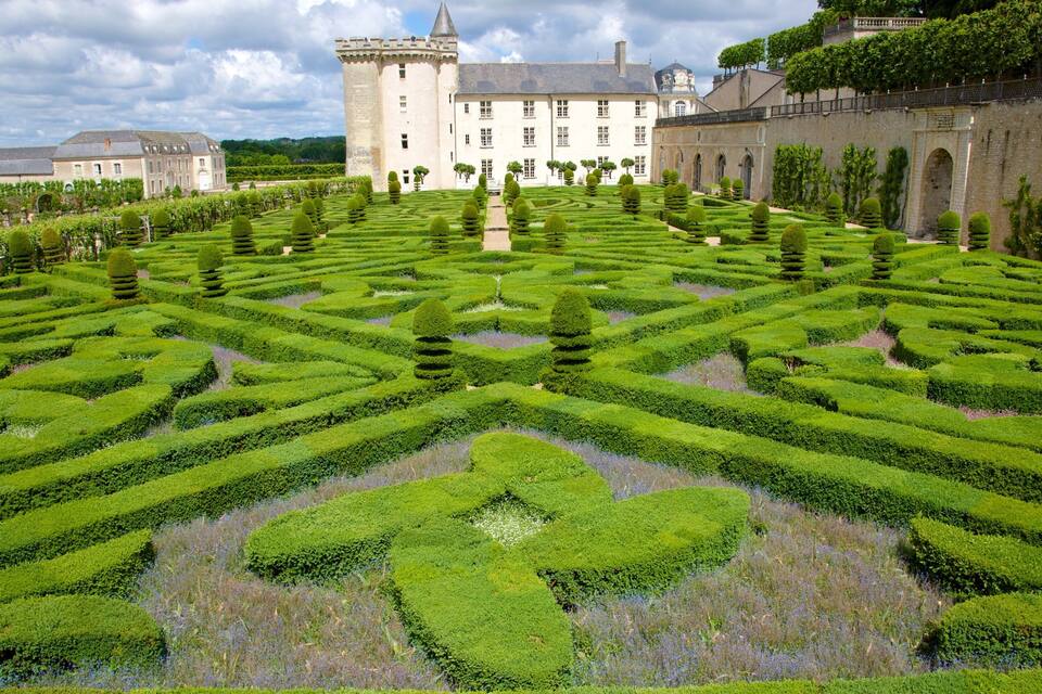 A formal garden with geometric patterns, a large castle, and a clear sky.