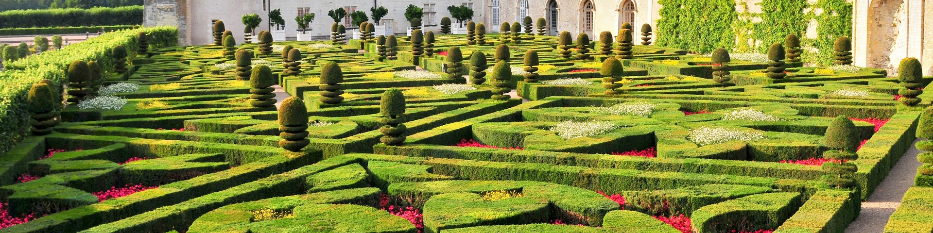 Um castelo com um jardim formal, apresentando sebes geométricas e um céu limpo.
