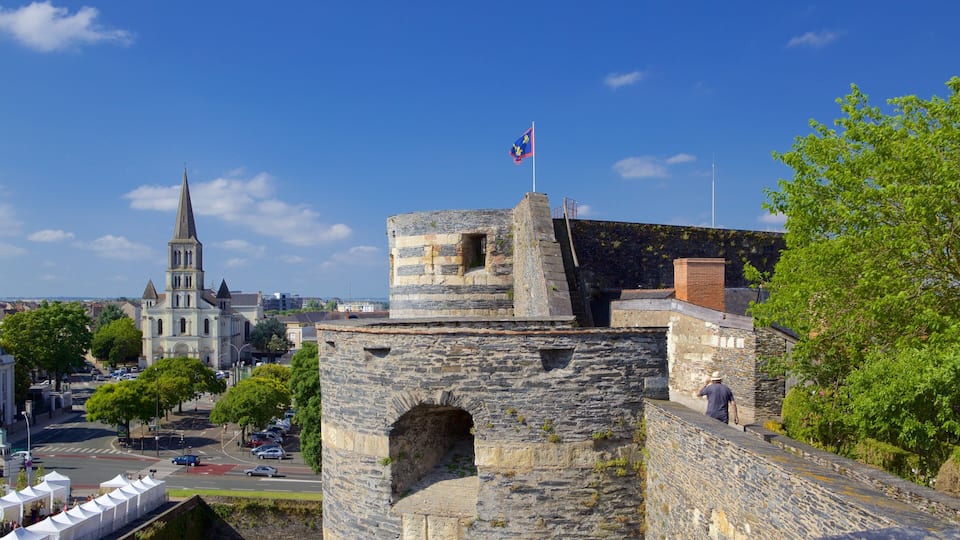 A historic stone tower with a flag, a church with a tall spire, and a modern cityscape in the background.