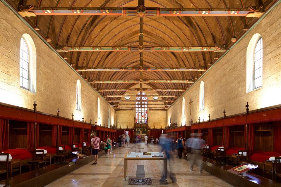 Een kerkinterieur met een hoog houten plafond, gewelfde ramen en rode gordijnen.