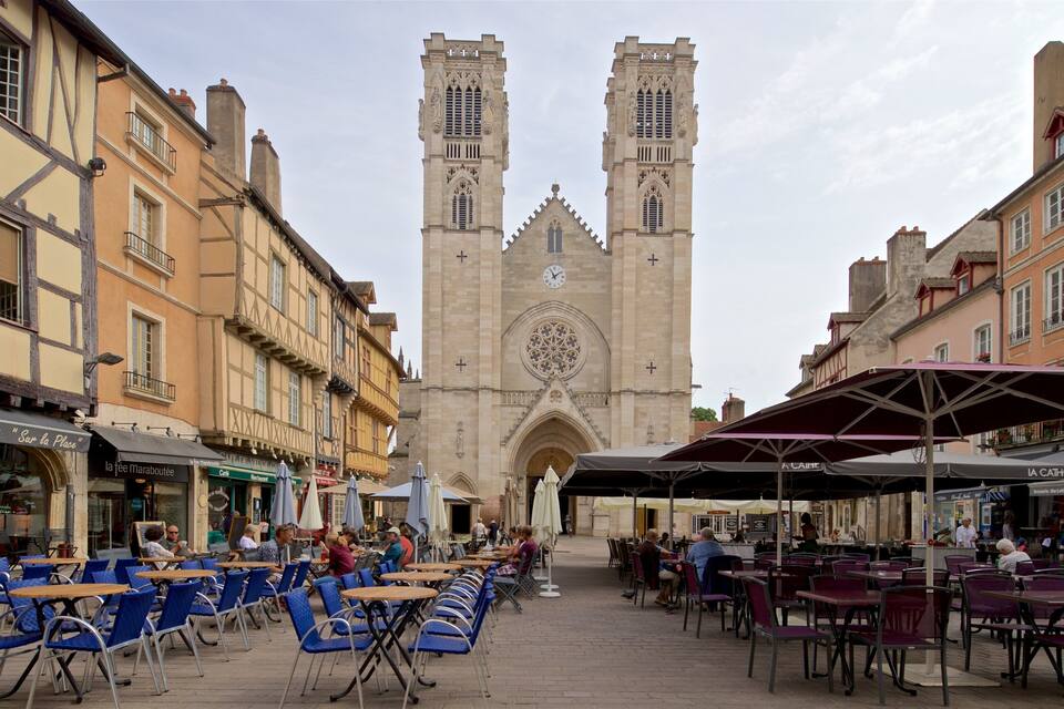 Une cathédrale historique, dotée de deux tours jumelles et d’une grande rosace. Devant, on trouve des cafés en plein air avec des tables et des chaises.