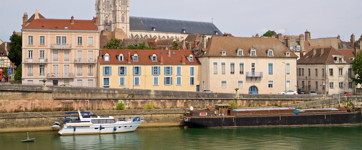 A river with boats, a large church, and colorful buildings along the riverbank.