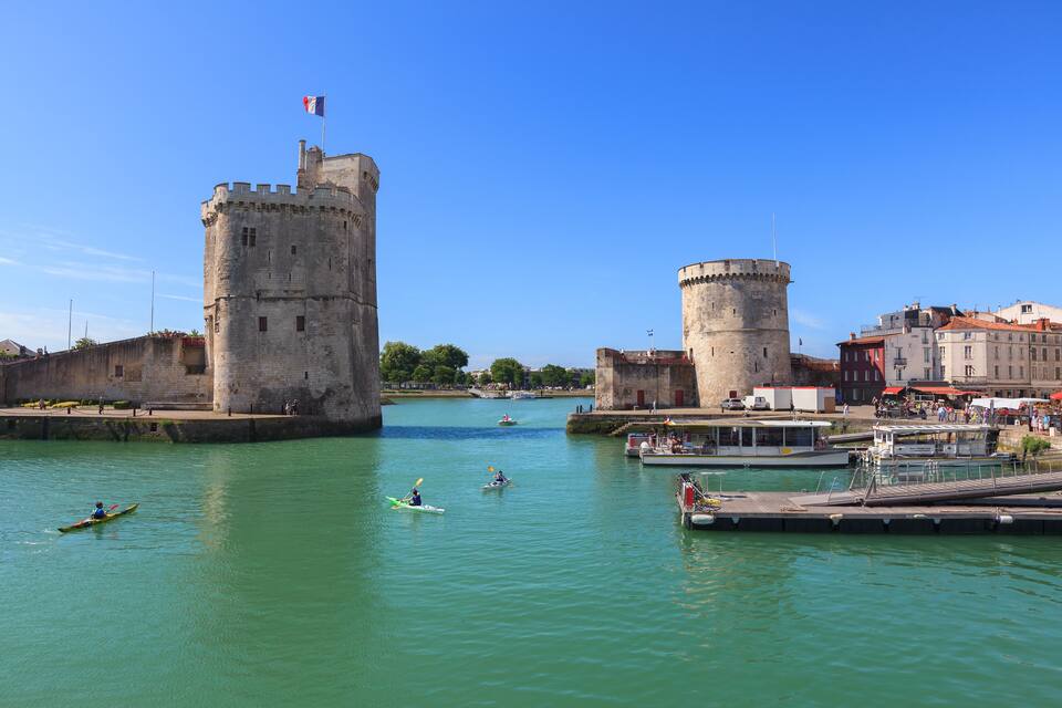 A historic castle with two towers, a calm river, and a small boat docked nearby.