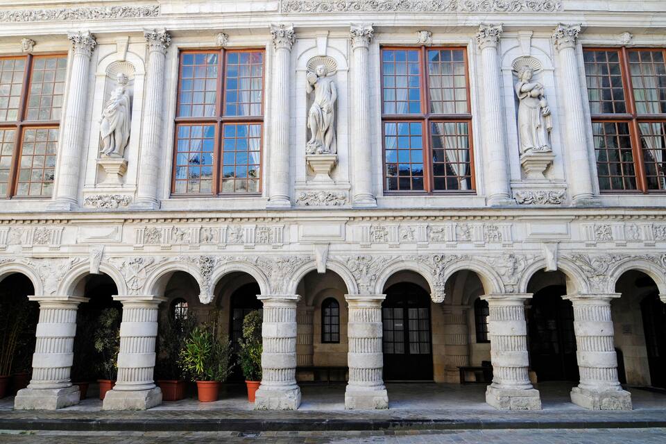 Une façade de style classique ornée de statues, de colonnes et de fenêtres en arc de cercle.