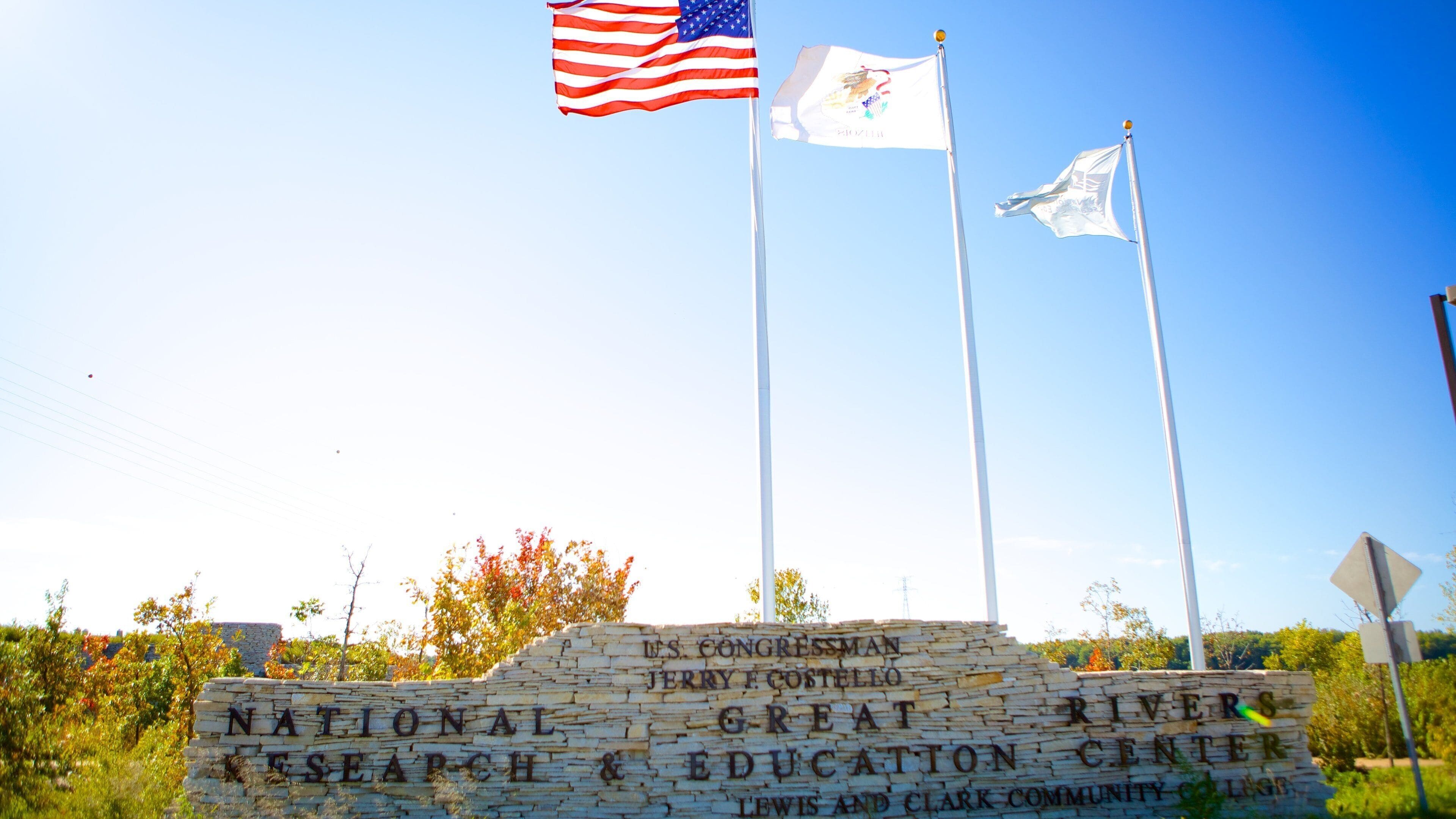 A sign for the National Great Rivers Center with three flags, including the American flag, in front of a stone wall.