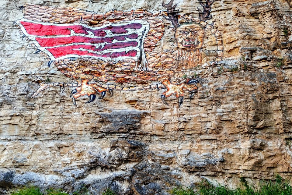 A rock face with a mural of a red and white striped flag, a deer, and a horse.