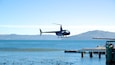 Een helikopter die boven water vliegt, met bergen op de achtergrond.