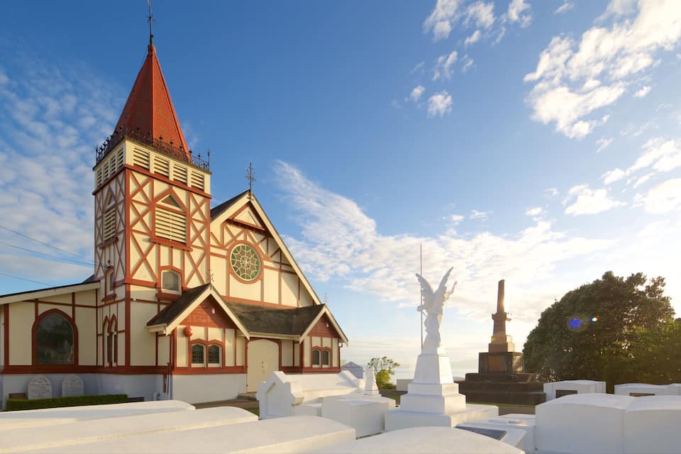 Une église dotée d’un clocher rouge et d’une façade blanche, entourée de pierres tombales blanches.