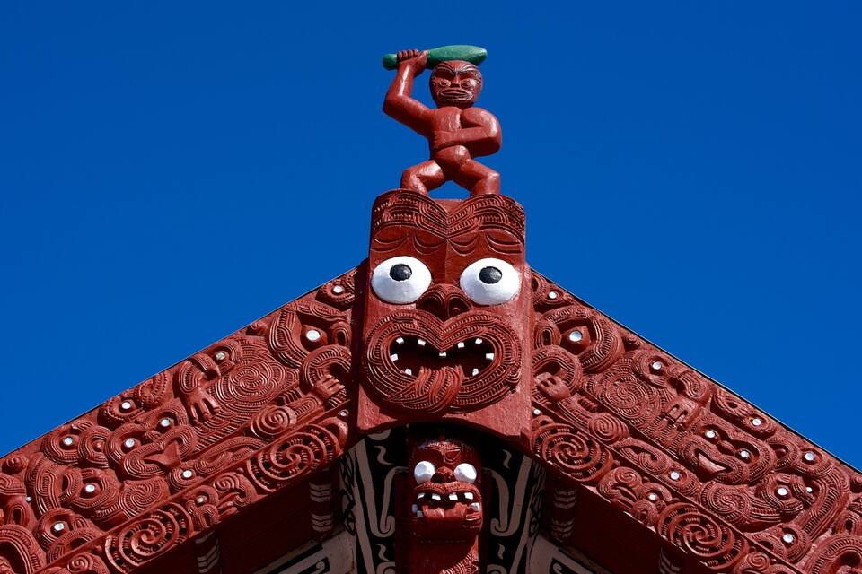 A red wooden structure with intricate carvings and a figure holding a green object.