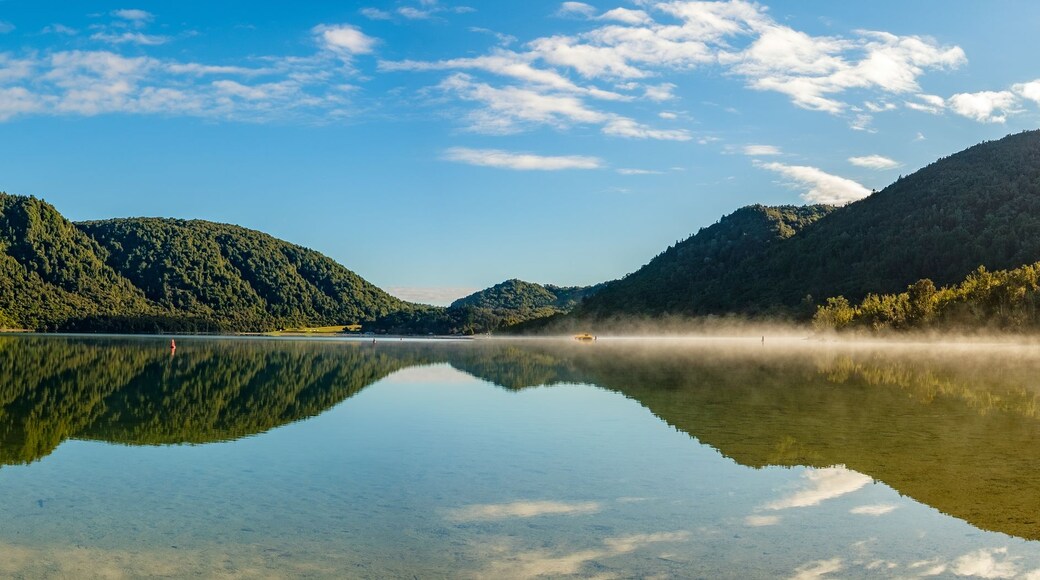 Ein ruhiger See mit dicht bewaldeten Hügeln und blauem Himmel.