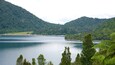 A lake surrounded by forested hills, with a clear sky.