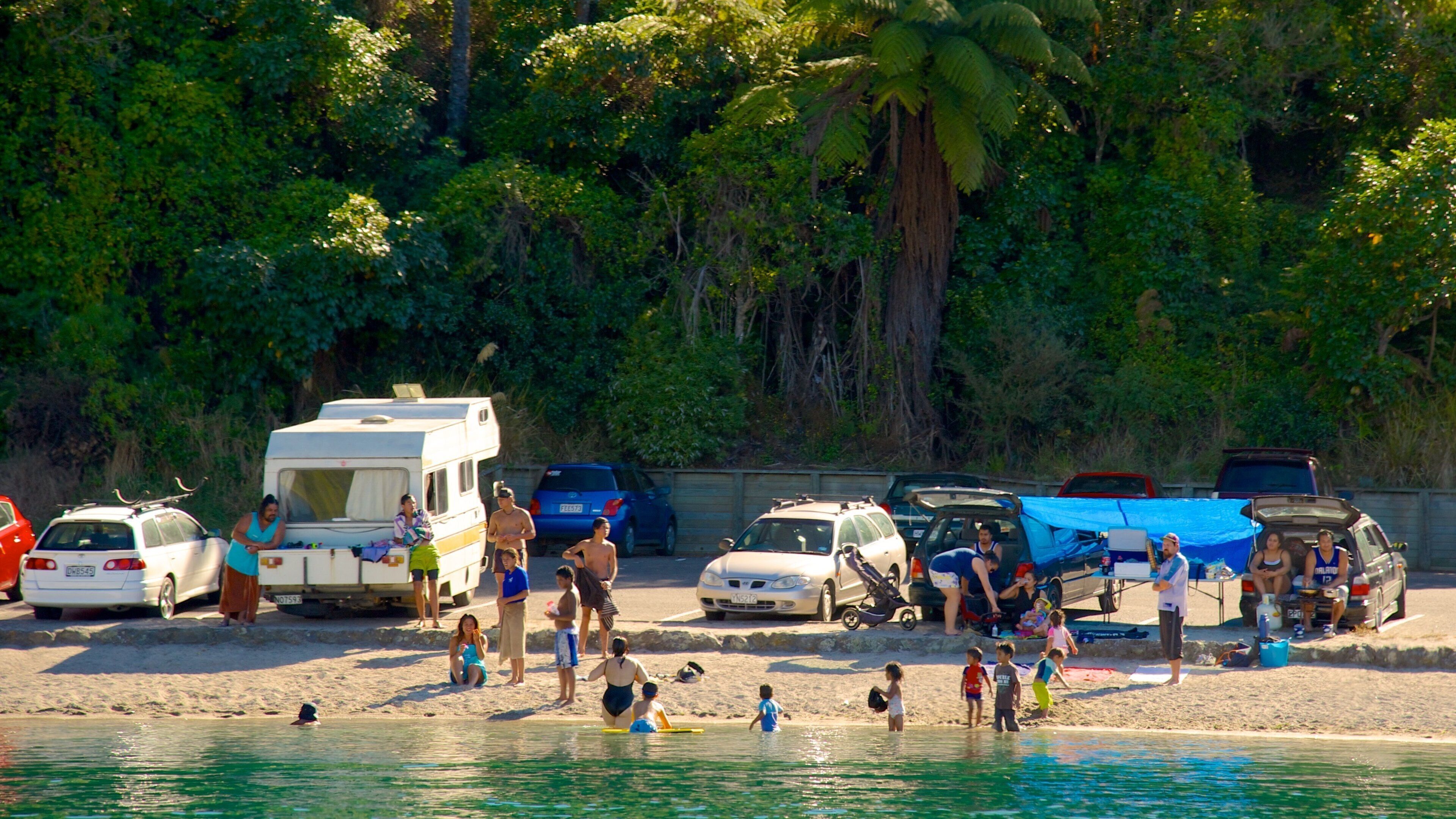 A beach with people, a caravan, and parked cars.