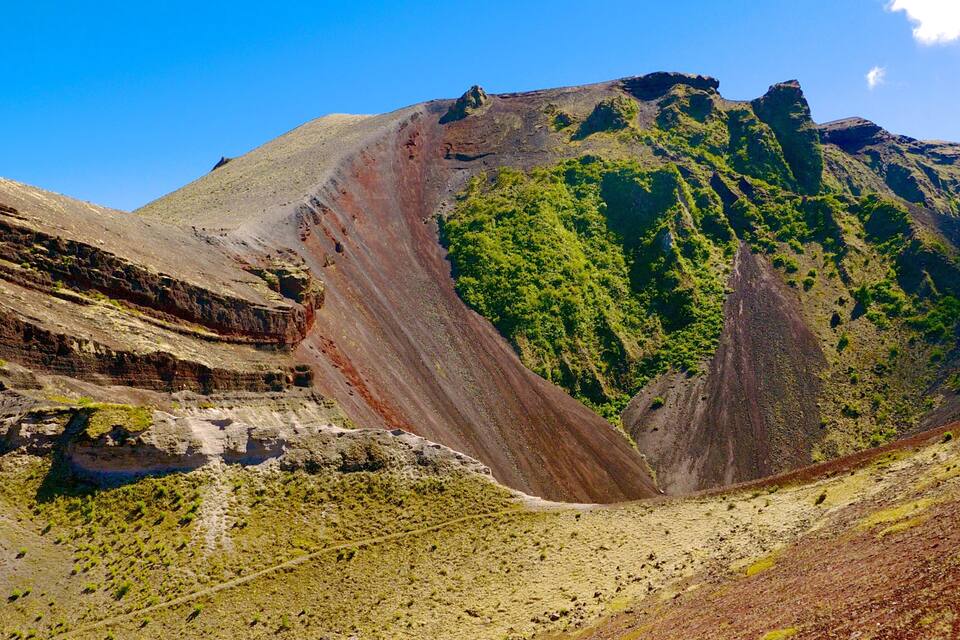 A rugged mountain landscape with layered rock formations and a green forested area.