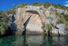 A rock formation with a carved face and a cave entrance surrounded by water and vegetation.