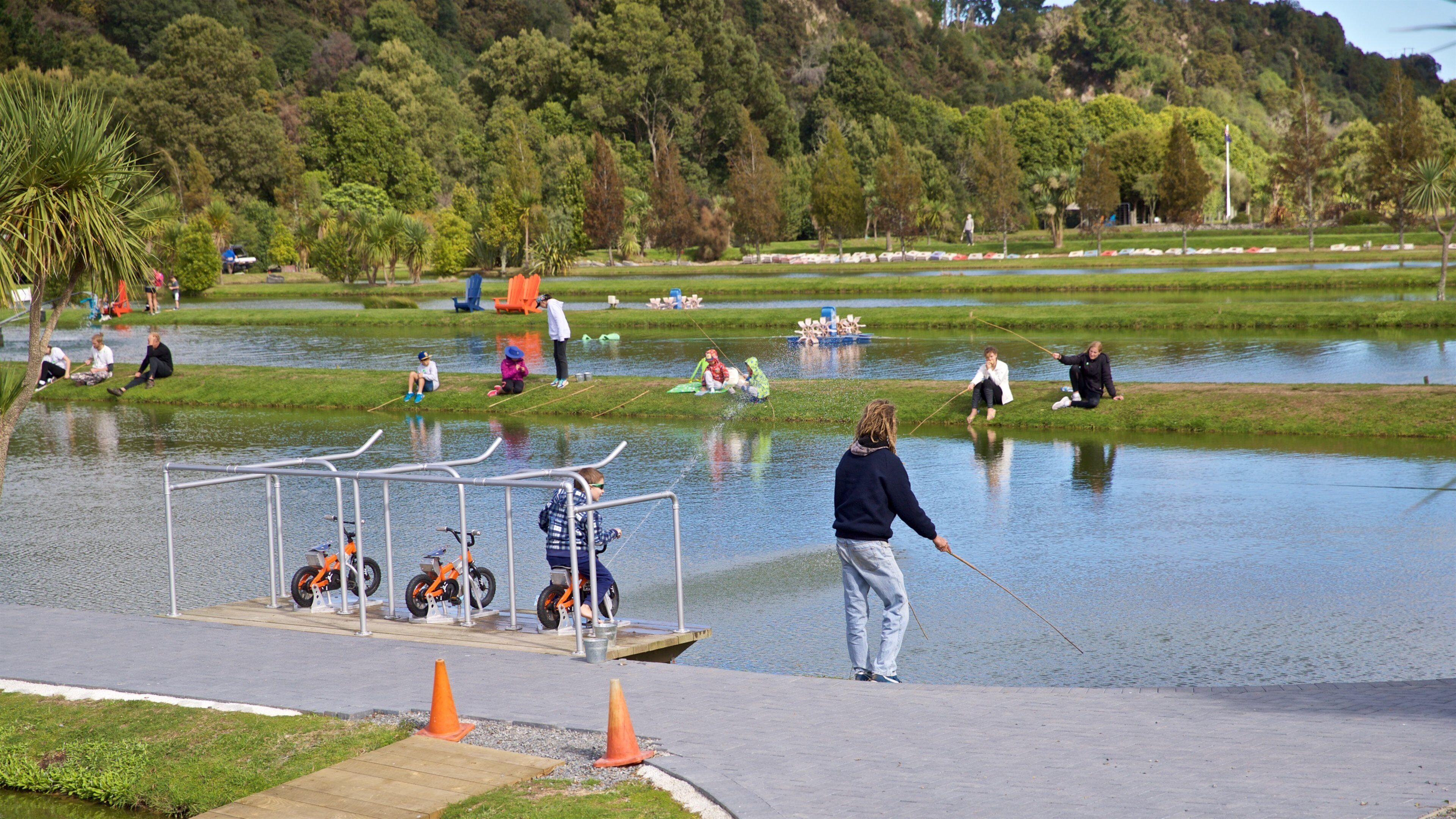 A lakeside park with people fishing and children playing near the water.