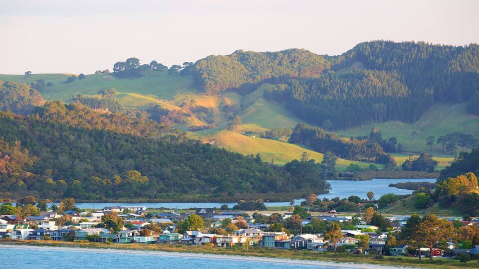 A coastal town with houses by the water, surrounded by hills and dense forests.