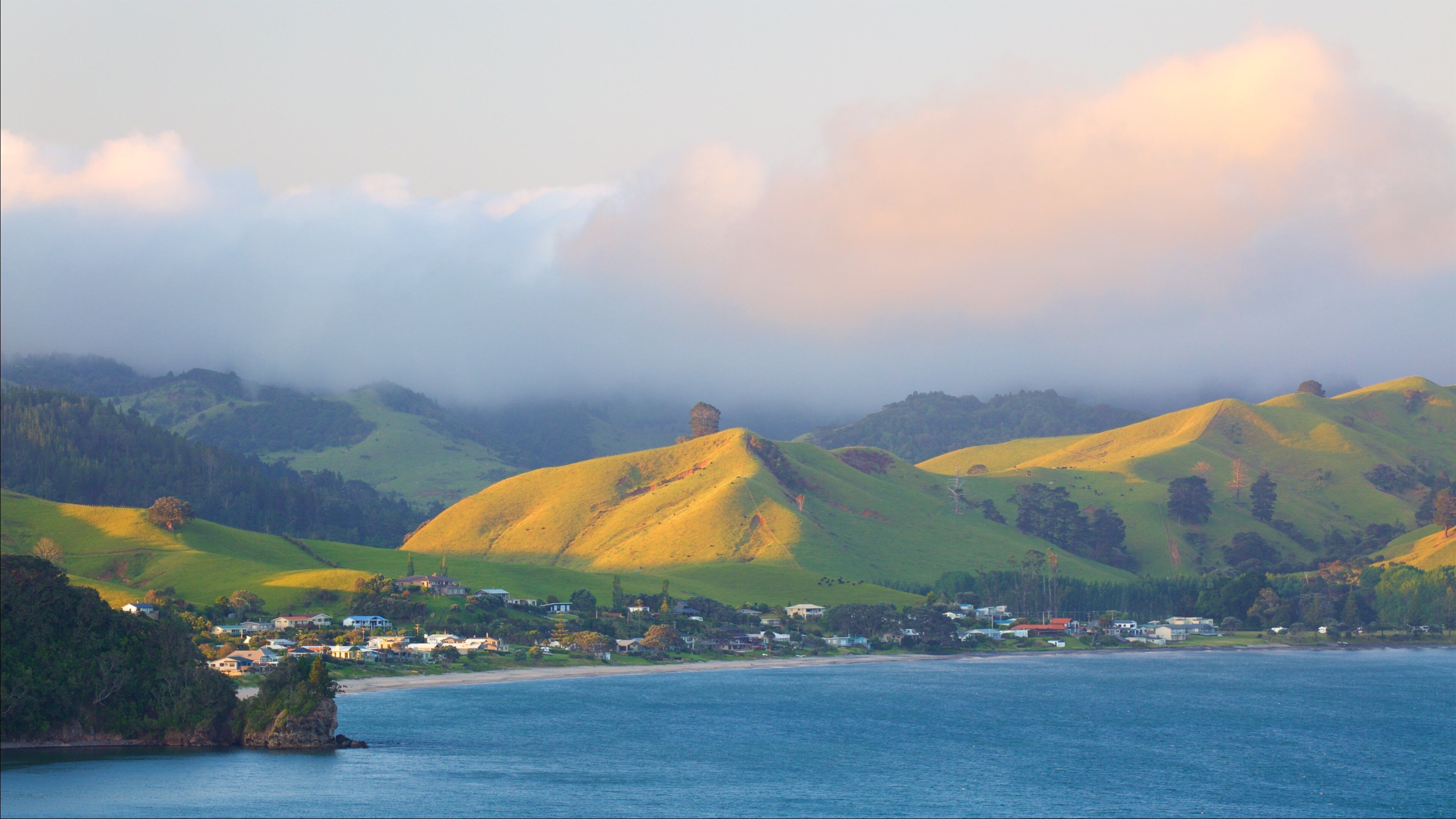 A coastal landscape with rolling hills, a small town, and a body of water.