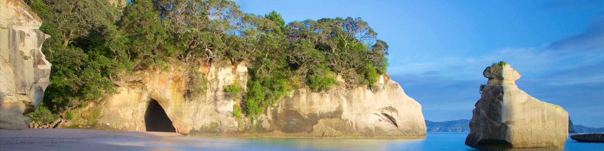 A coastal landscape with a prominent rock formation, a cave entrance, and lush greenery.