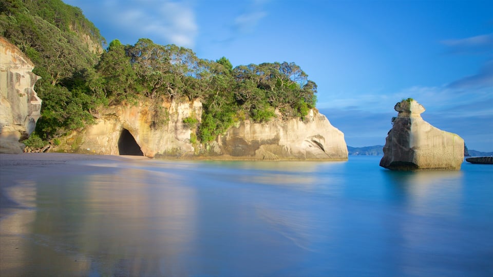 A coastal landscape with a prominent rock formation, a cave entrance, and lush greenery.
