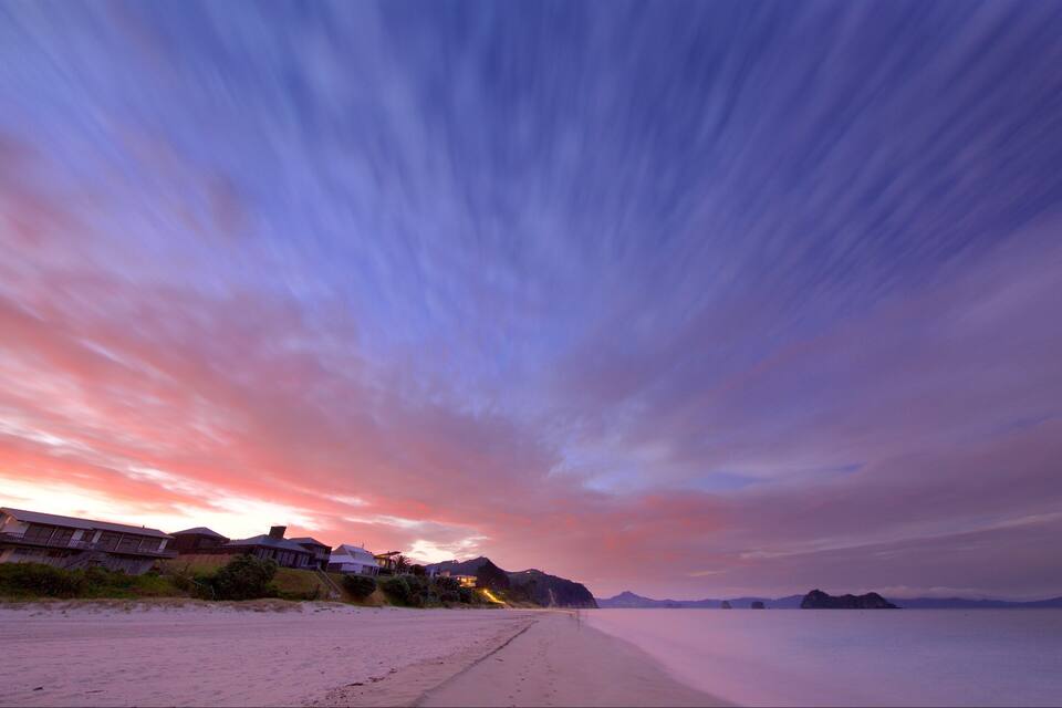 A beach with a sunset, houses, and distant mountains.
