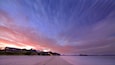 A beach with a sunset, houses, and distant mountains.