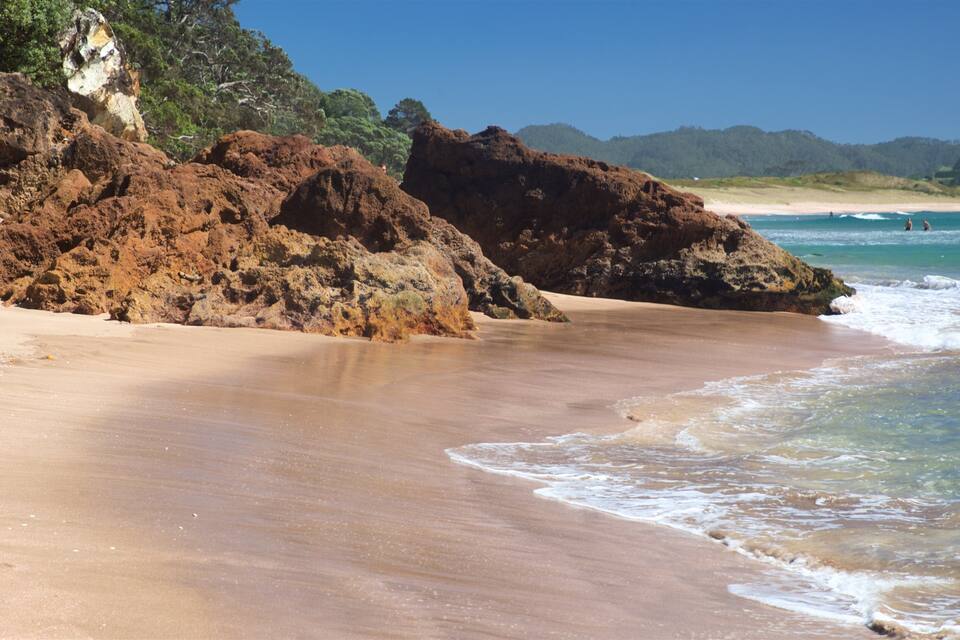 Uma praia arenosa com afloramentos rochosos e águas azul-claras.