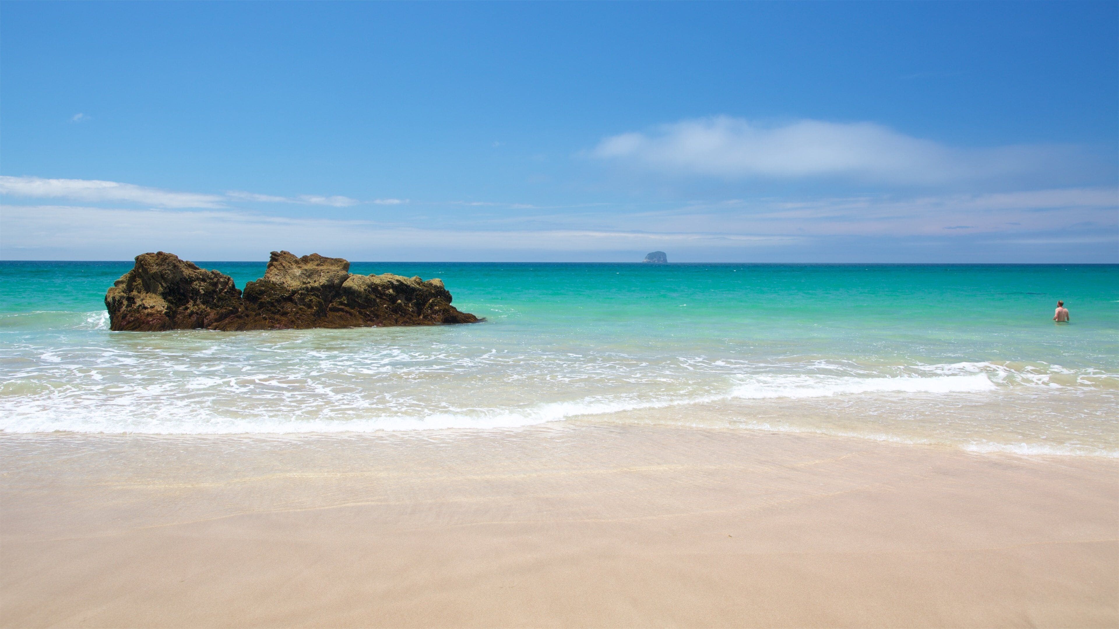 A sandy beach with clear turquoise water and a large rock formation.