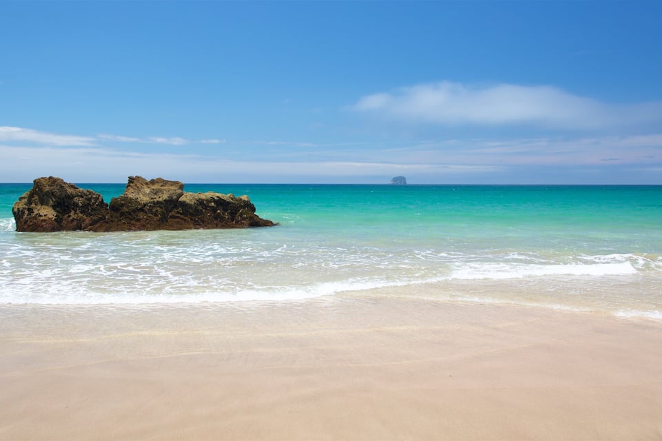 Uma praia arenosa com águas turquesa cristalinas e uma grande formação rochosa.