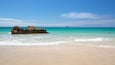 A sandy beach with clear turquoise water and a large rock formation.