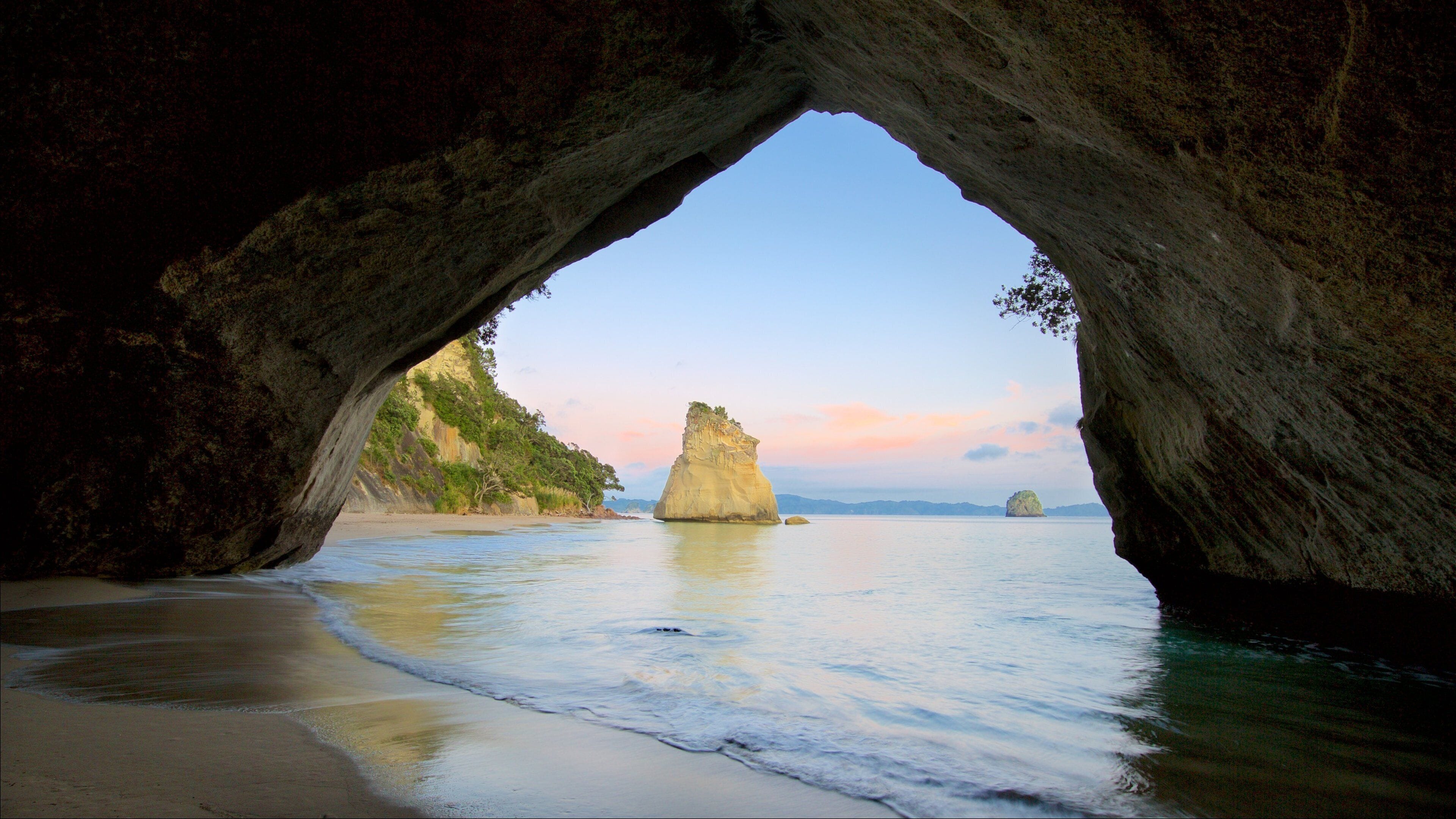 A natural rock arch over a beach with calm waters and distant islands.