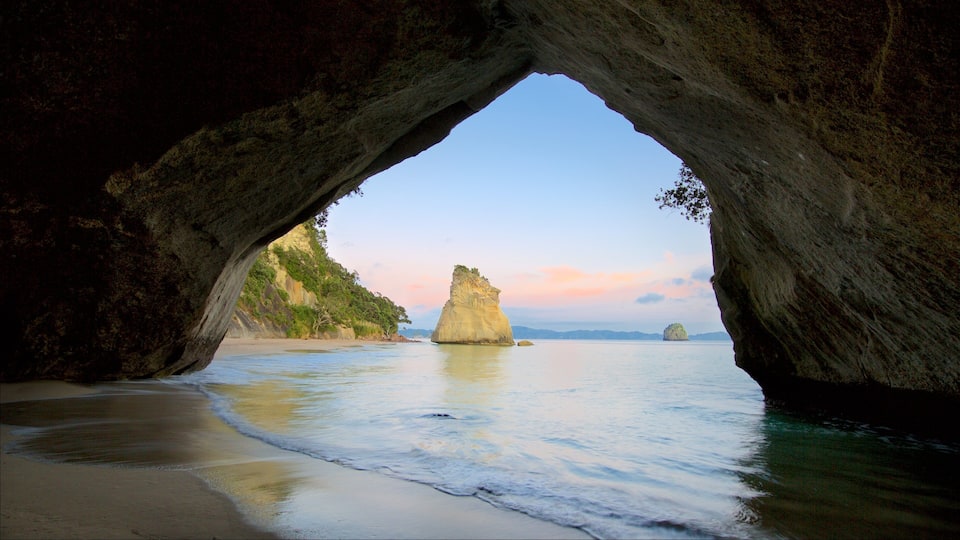 A natural rock arch over a beach with calm waters and distant islands.