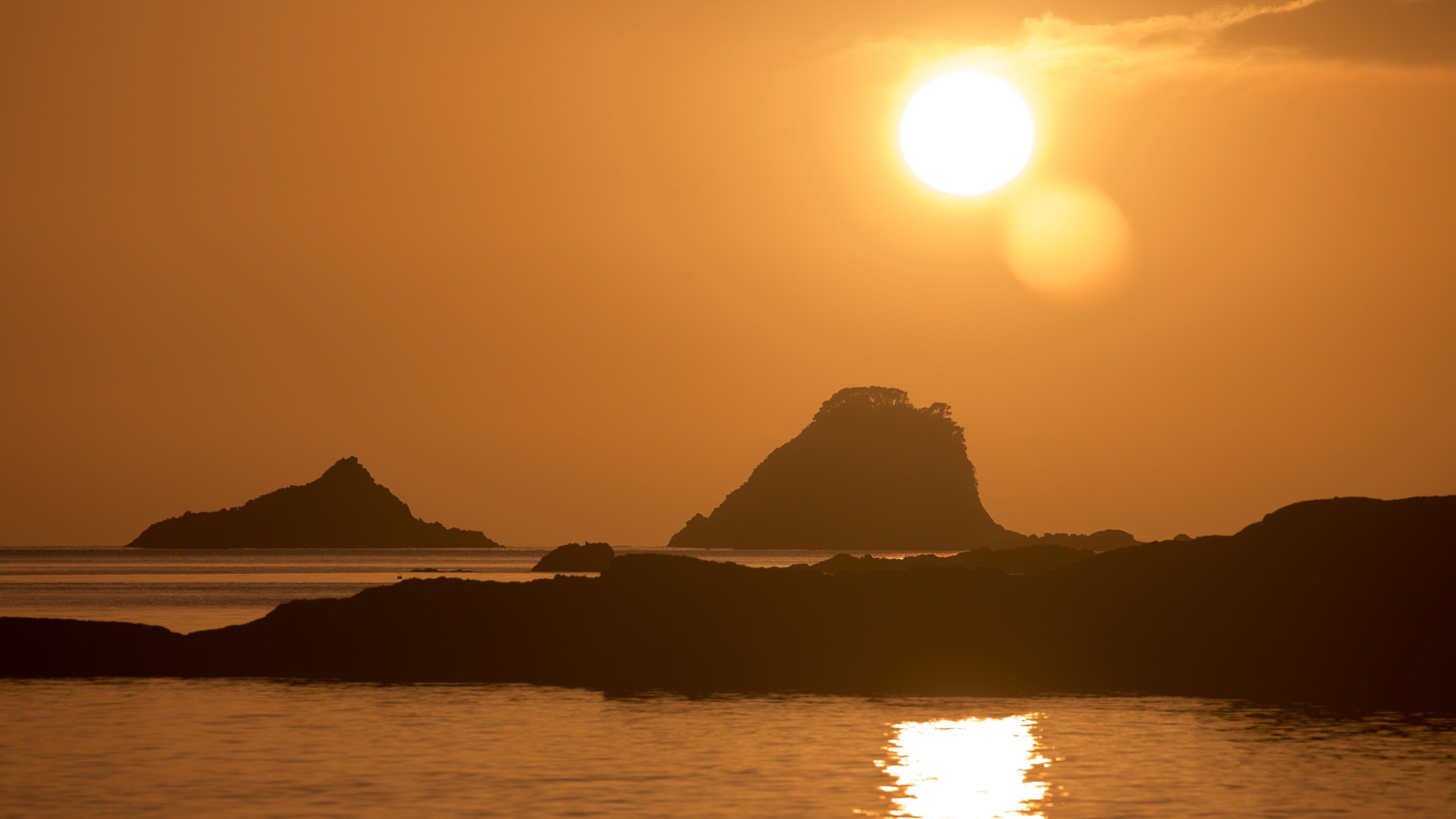 A sunset over a coastal landscape with prominent rock formations silhouetted against the sky.