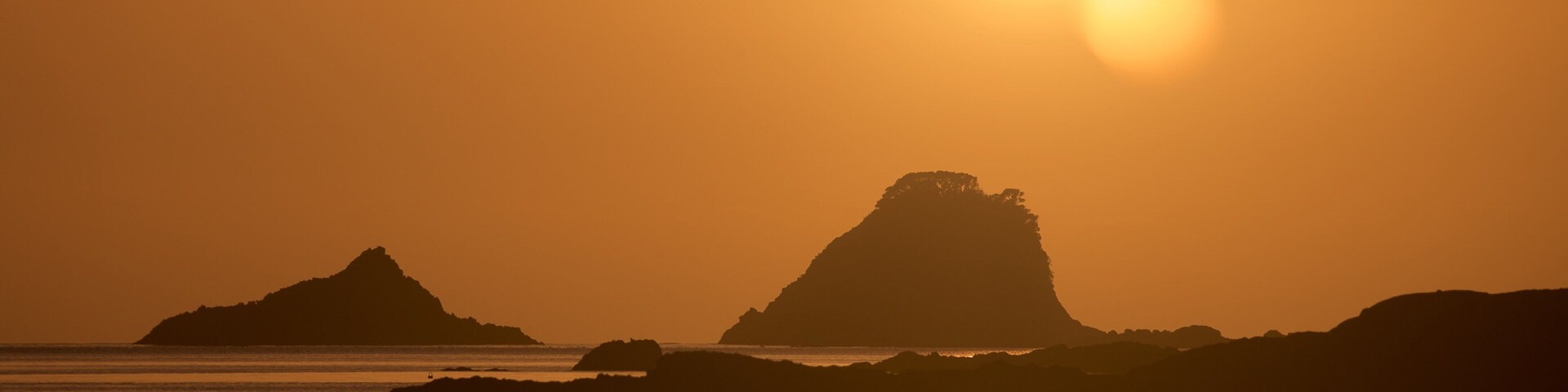 A sunset over a coastal landscape with prominent rock formations silhouetted against the sky.