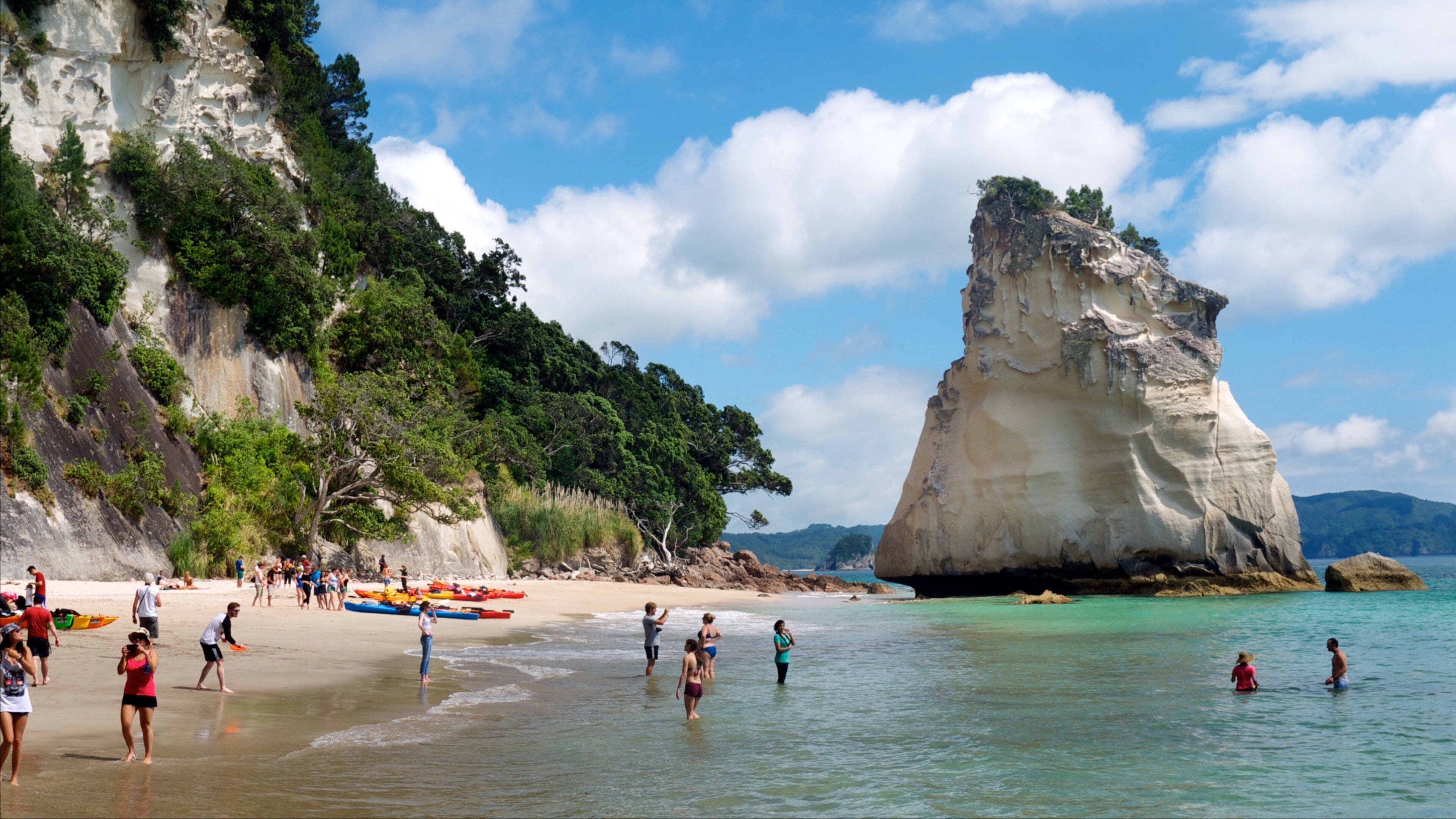 A beach with people, kayaks, and a large rock formation.