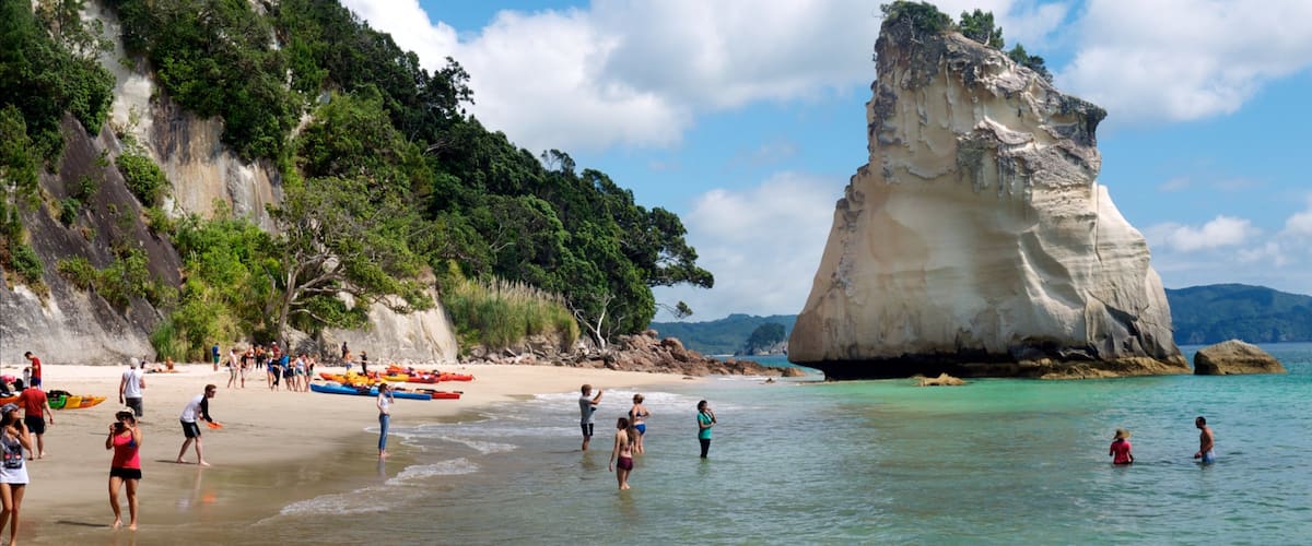 A beach with people, kayaks, and a large rock formation.