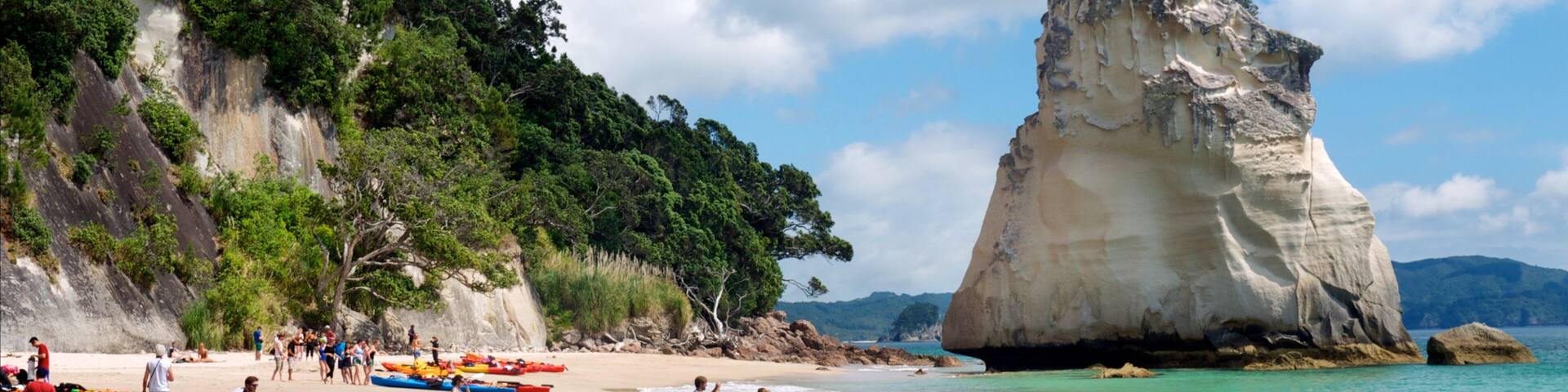 A beach with people, kayaks, and a large rock formation.