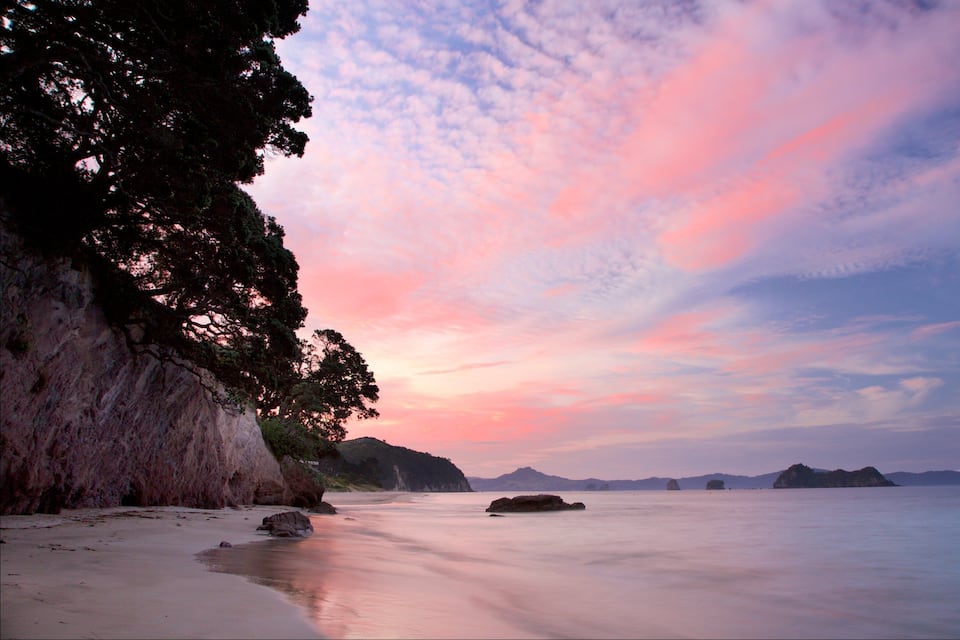 A beach with a rocky cliff and calm water.
