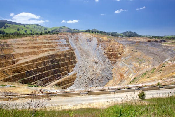Une vaste mine à ciel ouvert, avec des parois en terrasses et un train circulant sur des voies ferrées au premier plan.