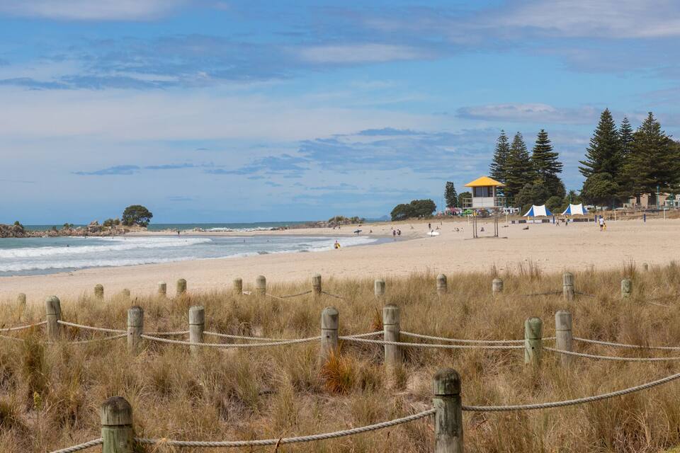 A beach with a wooden fence, grassy dunes, and a forested hill in the background.