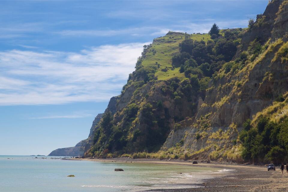 A coastal landscape with a beach, rocky cliffs, and a clear sky.