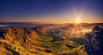 Paisagem montanhosa com vale e rio ao pôr do sol.