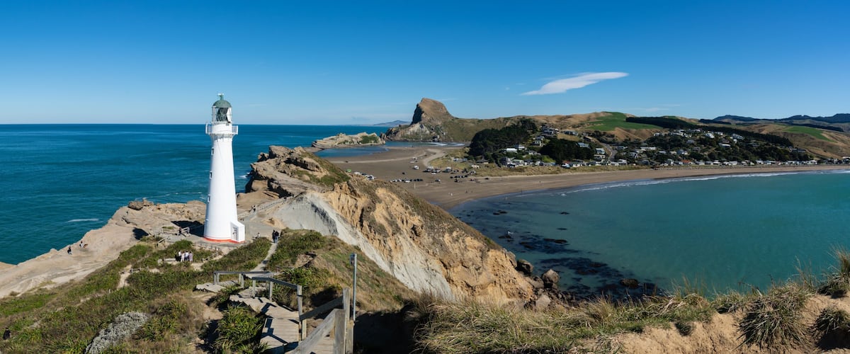 A coastal landscape with a prominent white lighthouse, a sandy beach, and a rocky cliff overlooking the ocean.