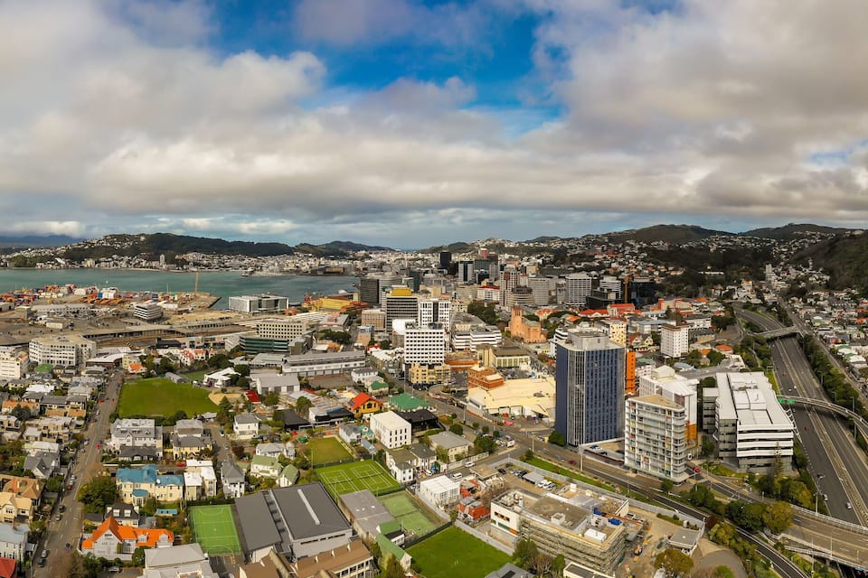 A coastal cityscape with a stadium, dense urban buildings, and a mountainous backdrop.