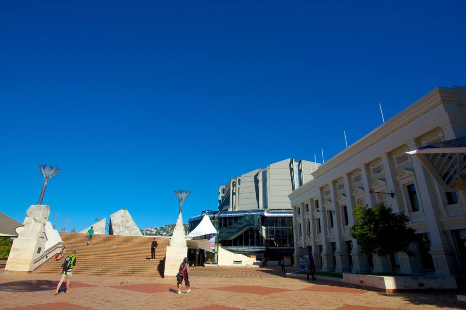 A plaza with modern buildings, a large sculpture, and a clear blue sky.
