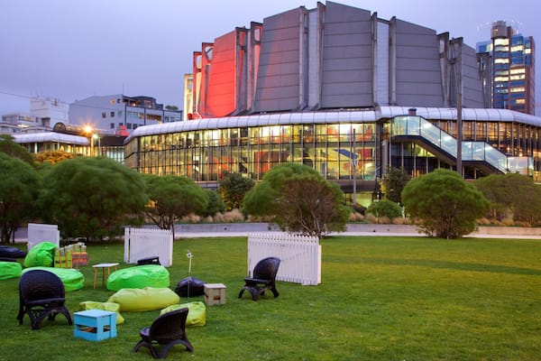 A modern building with a glass facade and a curved roof, surrounded by a grassy area with colorful bean bags and a white picket fence.