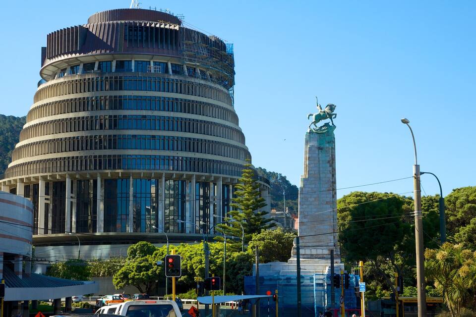A modern building with a cylindrical design, a tall monument with a statue, and a busy intersection with traffic lights.